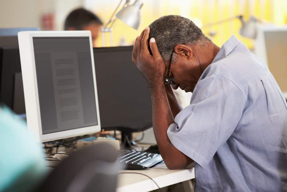 Stressed Man Working At Desk In Busy Creative Office