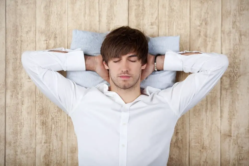 Businessman With Hands Behind Head Sleeping On Wooden Wall