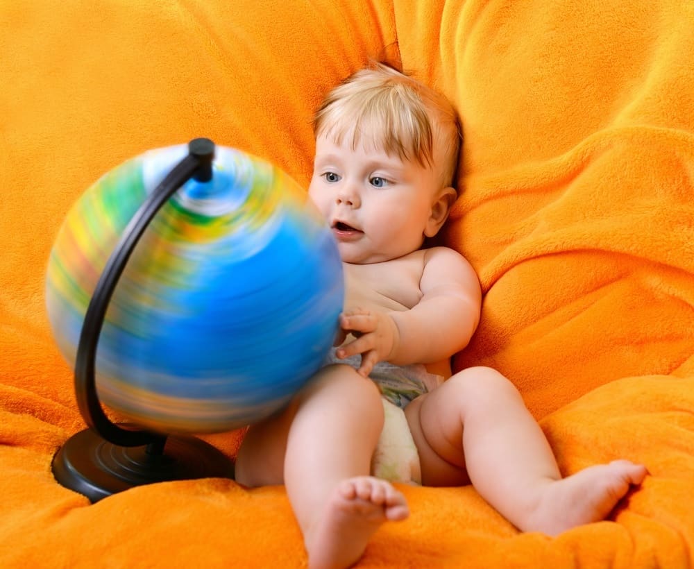 Happy smiling baby boy playing with terrestrial globe sitting on